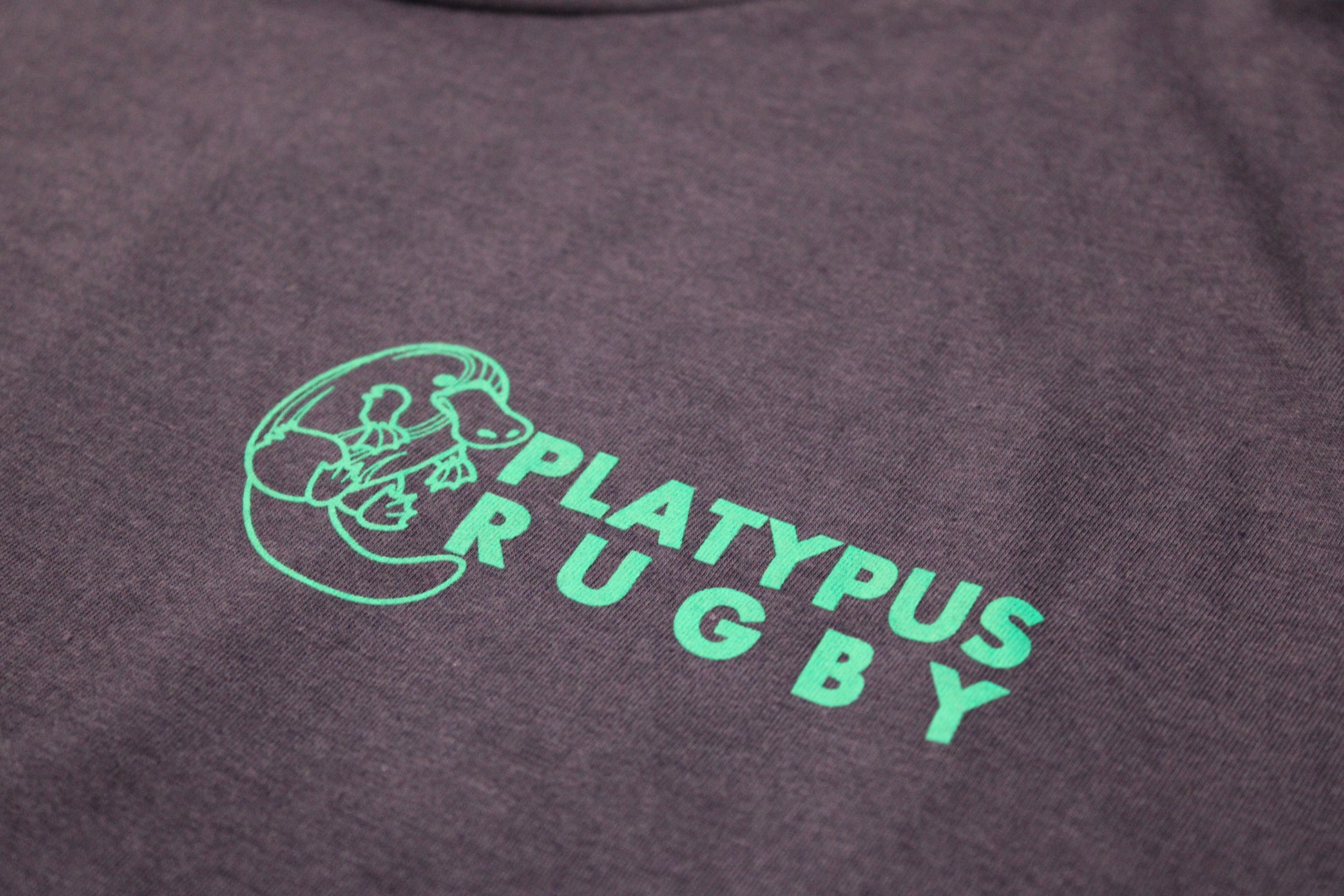 Platypus Rugby logo in teal on a dark fabric background
